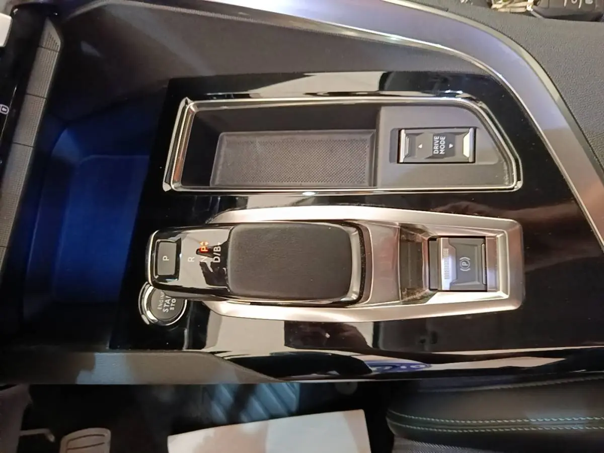 Vue rapprochée de la console centrale noire brillante du Peugeot 3008 1.6 HYBRID 225 avec levier de vitesses et bouton mode.