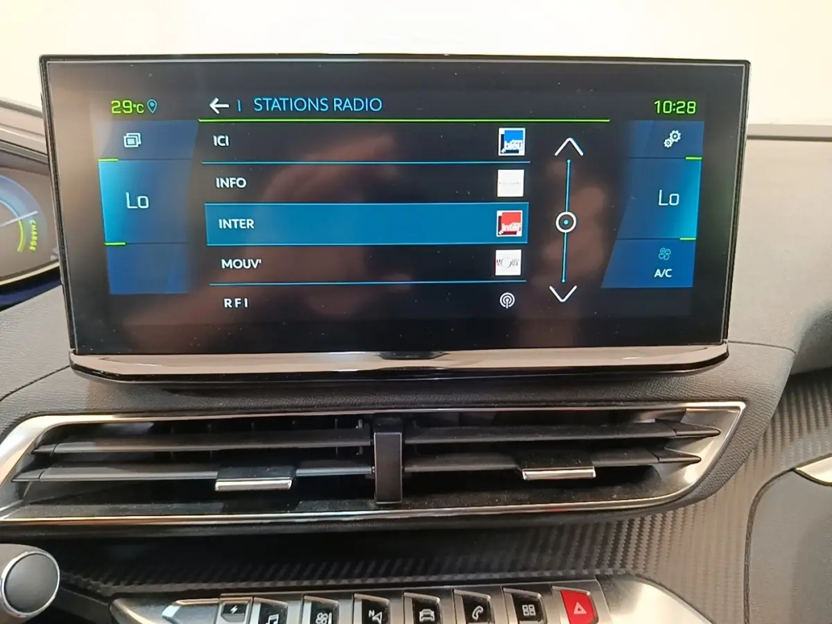 Écran tactile central affichant les stations radio dans l’habitacle du Peugeot 3008 hybride bleu, vue frontale rapprochée.