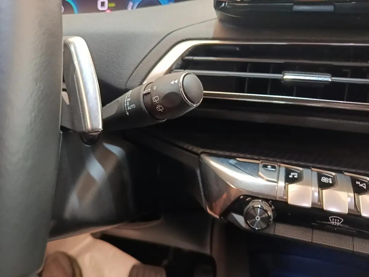 Détail intérieur du Peugeot 3008 hybride 2023 montrant la commande des essuie-glaces et les boutons de la console centrale.
