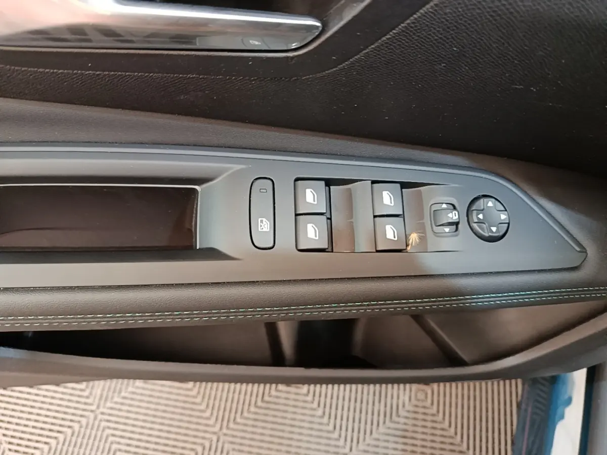 Gros plan sur la commande des vitres côté gauche en cuir noir avec surpiqûres bleues du Peugeot 3008 hybride bleu 2023.