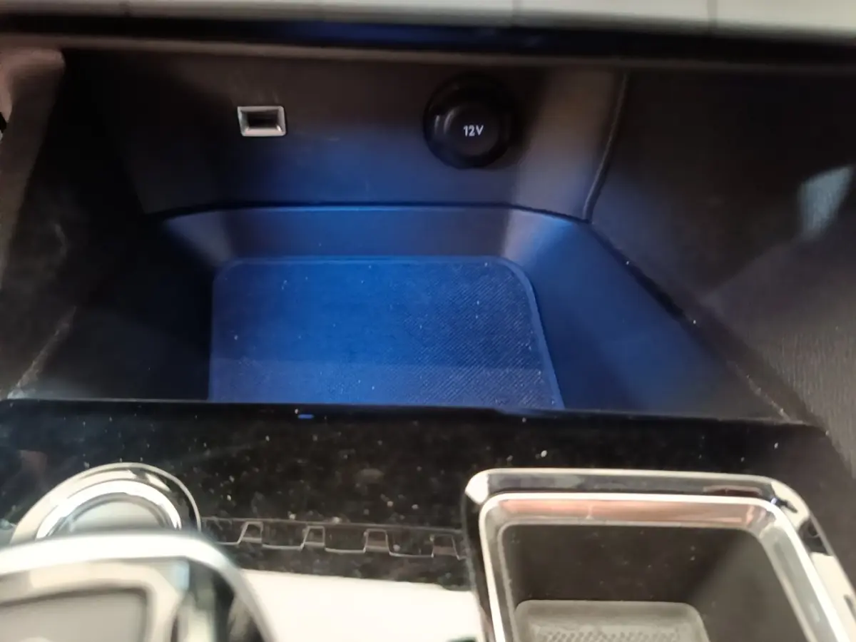 Gros plan sur la console centrale noire du Peugeot 3008 hybride 2023 avec prise 12V et port USB visible.
