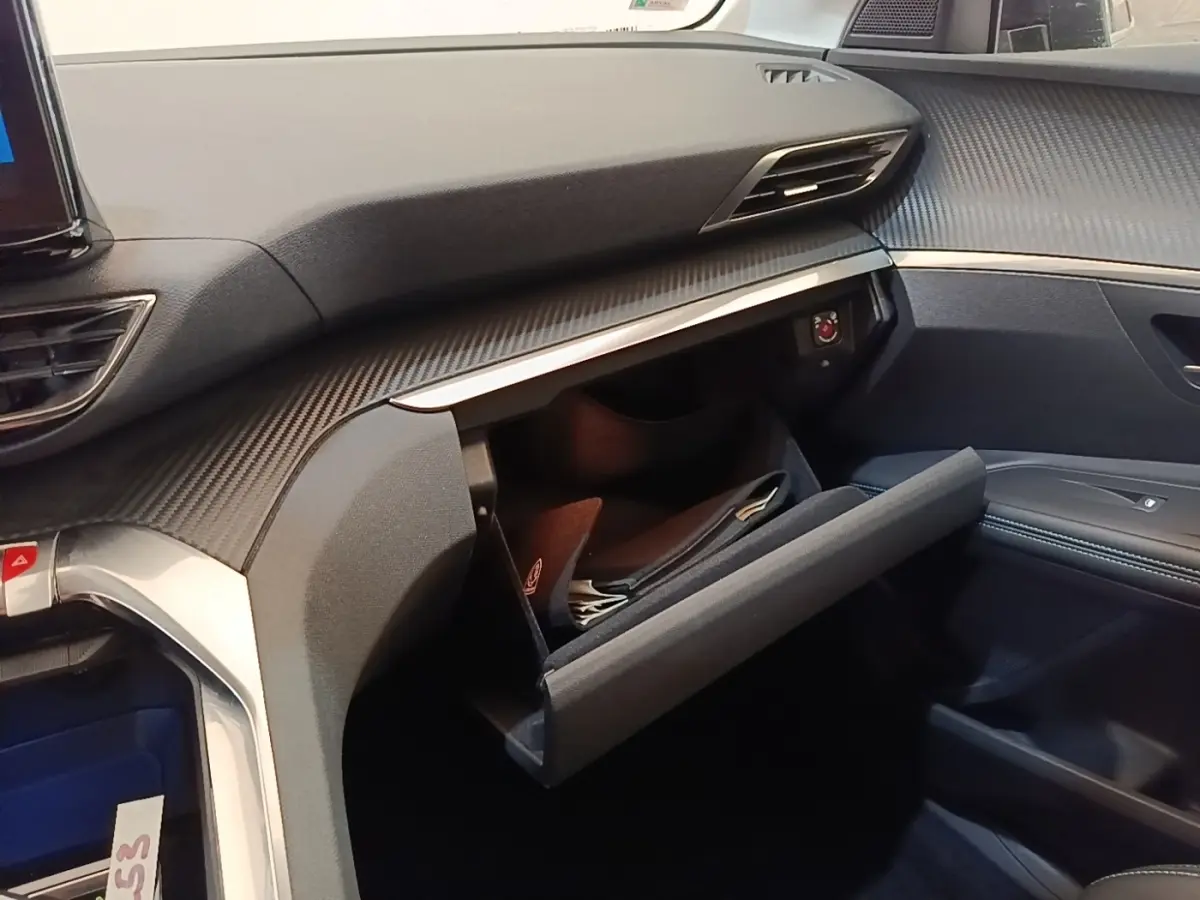 Intérieur du Peugeot 3008 hybride 2023, vue côté passager sur la boîte à gants ouverte et tableau de bord noir texturé.