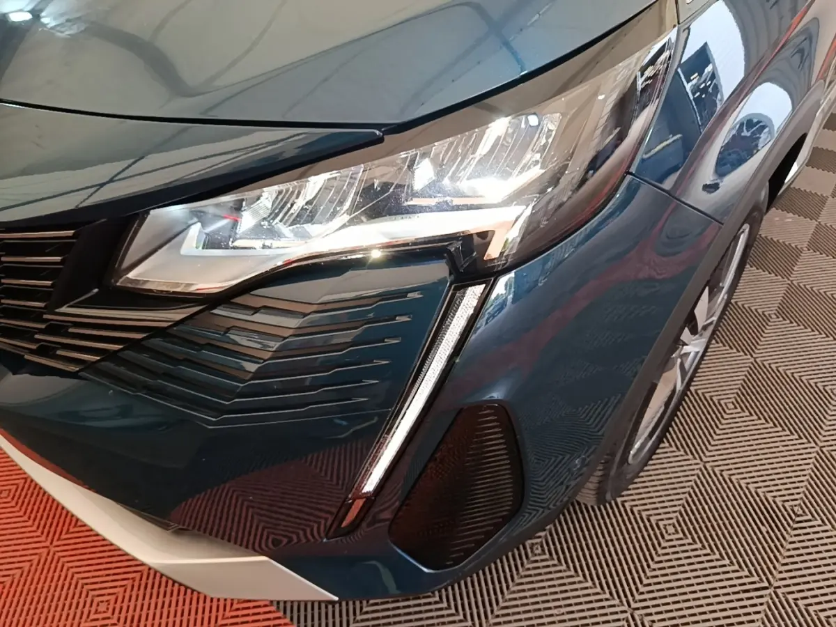 Gros plan sur l'avant droit bleu du Peugeot 3008 1.6 HYBRID 225 avec phare LED et calandre distinctive.