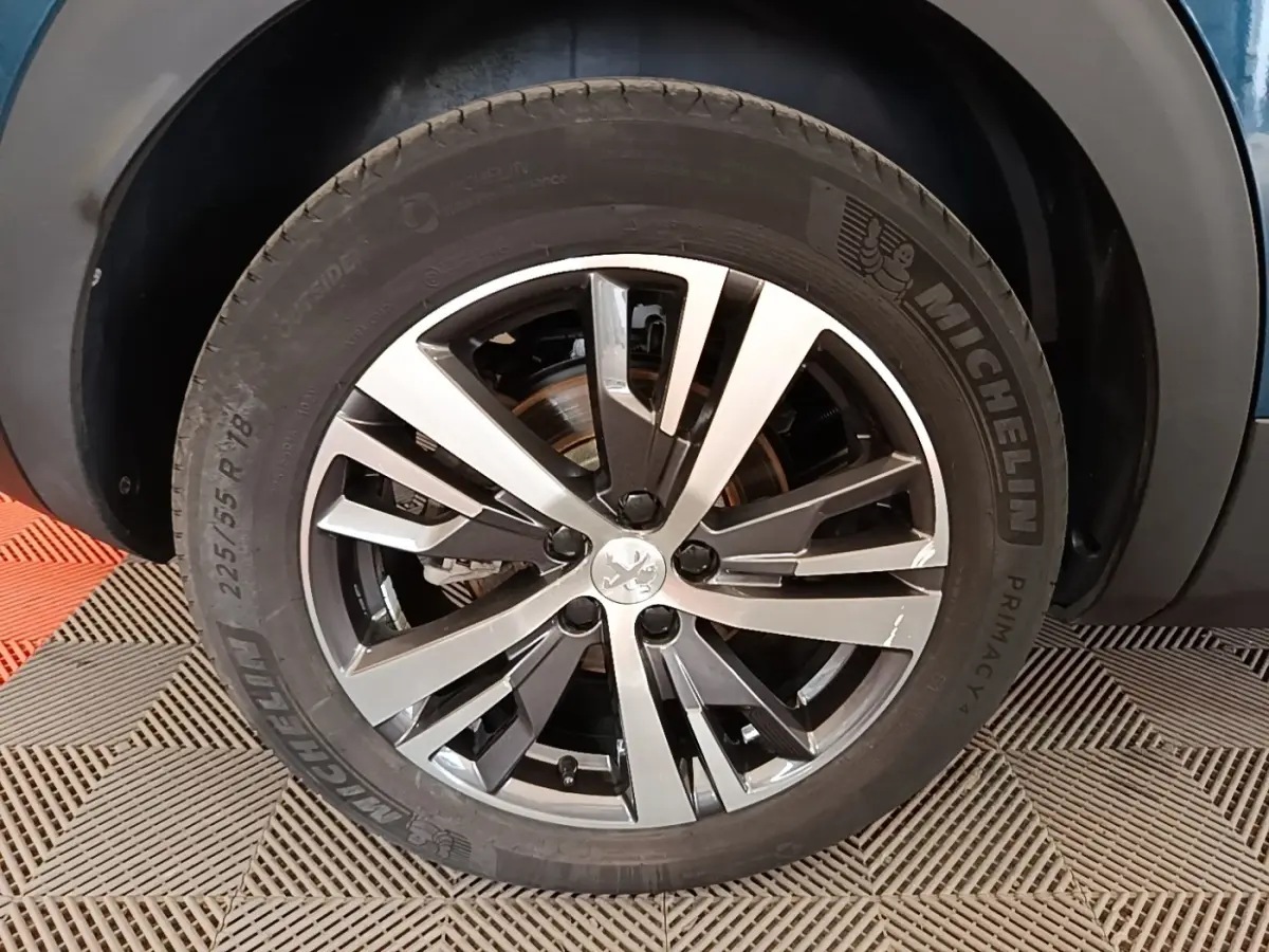Gros plan sur la roue avant gauche du Peugeot 3008 bleu 2023, jante alliage bicolore et pneu Michelin.