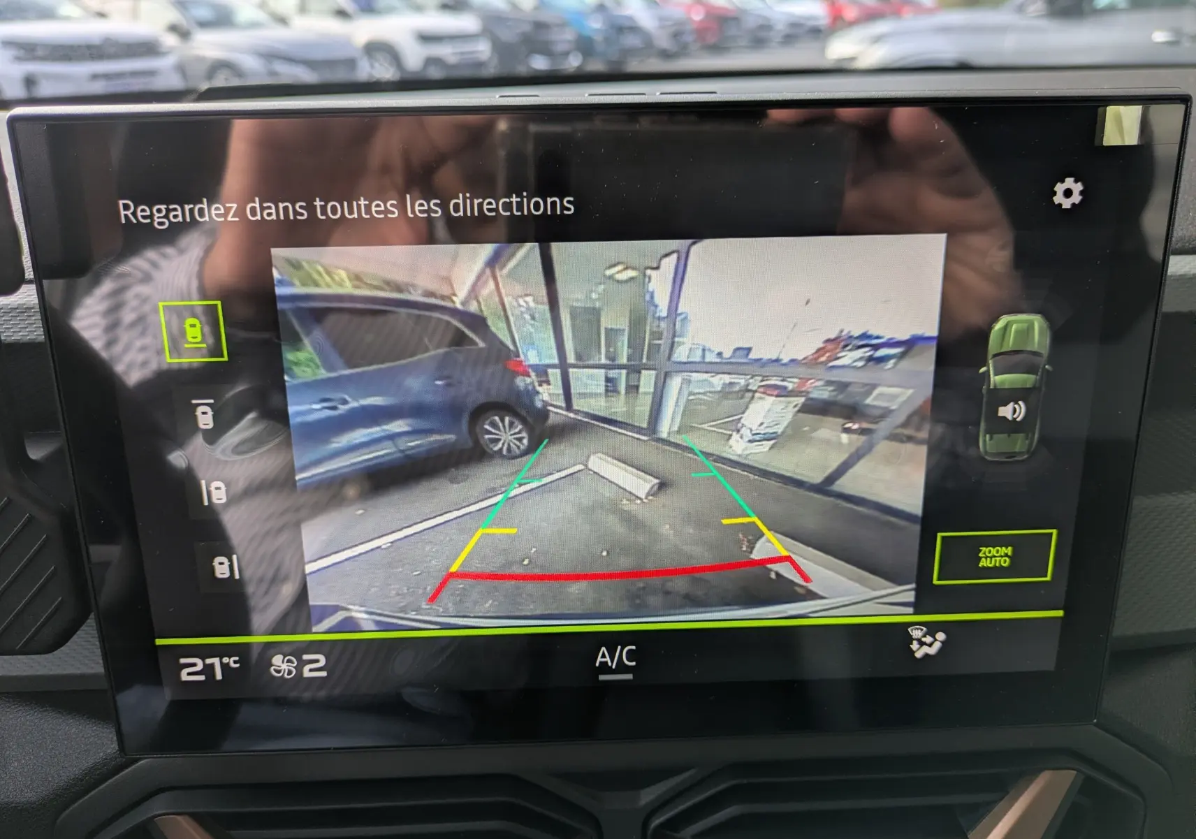 Écran intérieur montrant la caméra de recul du Dacia Duster blanc glacier, avec guidage de trajectoire coloré.