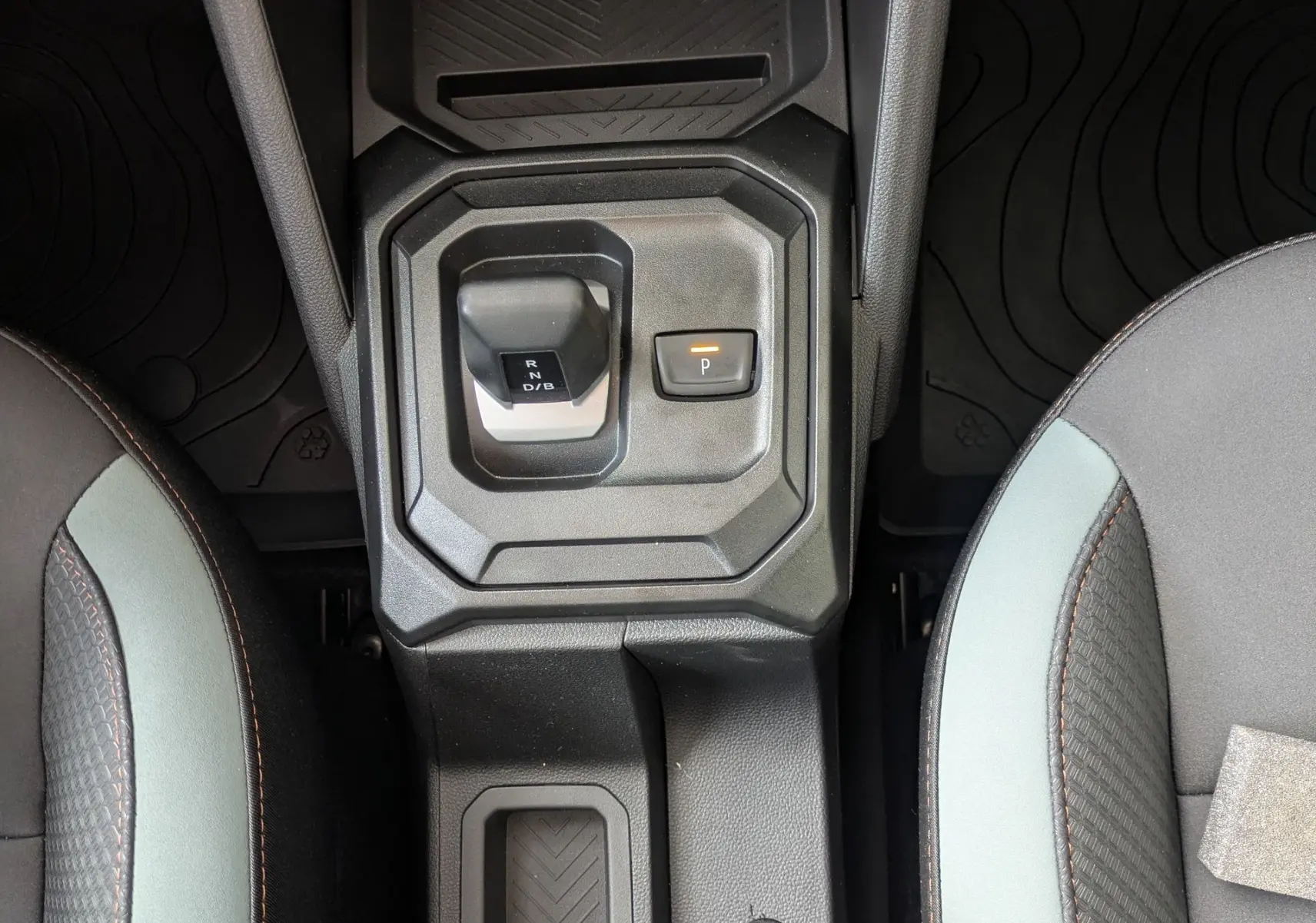 Vue plongeante sur la console centrale du Dacia Duster Hybrid 155 Extreme, avec levier de vitesses et sièges bicolores gris et noir.