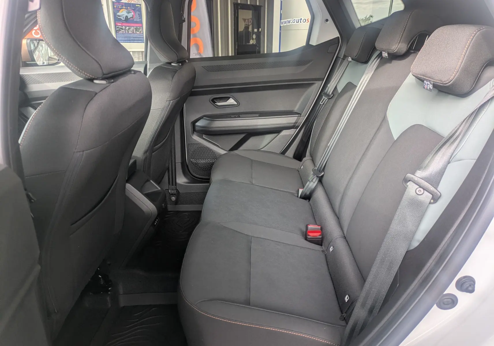 Vue latérale intérieure arrière droite du Dacia Duster Hybrid 155 Extreme 2026, sièges tissu noir avec surpiqûres orange.