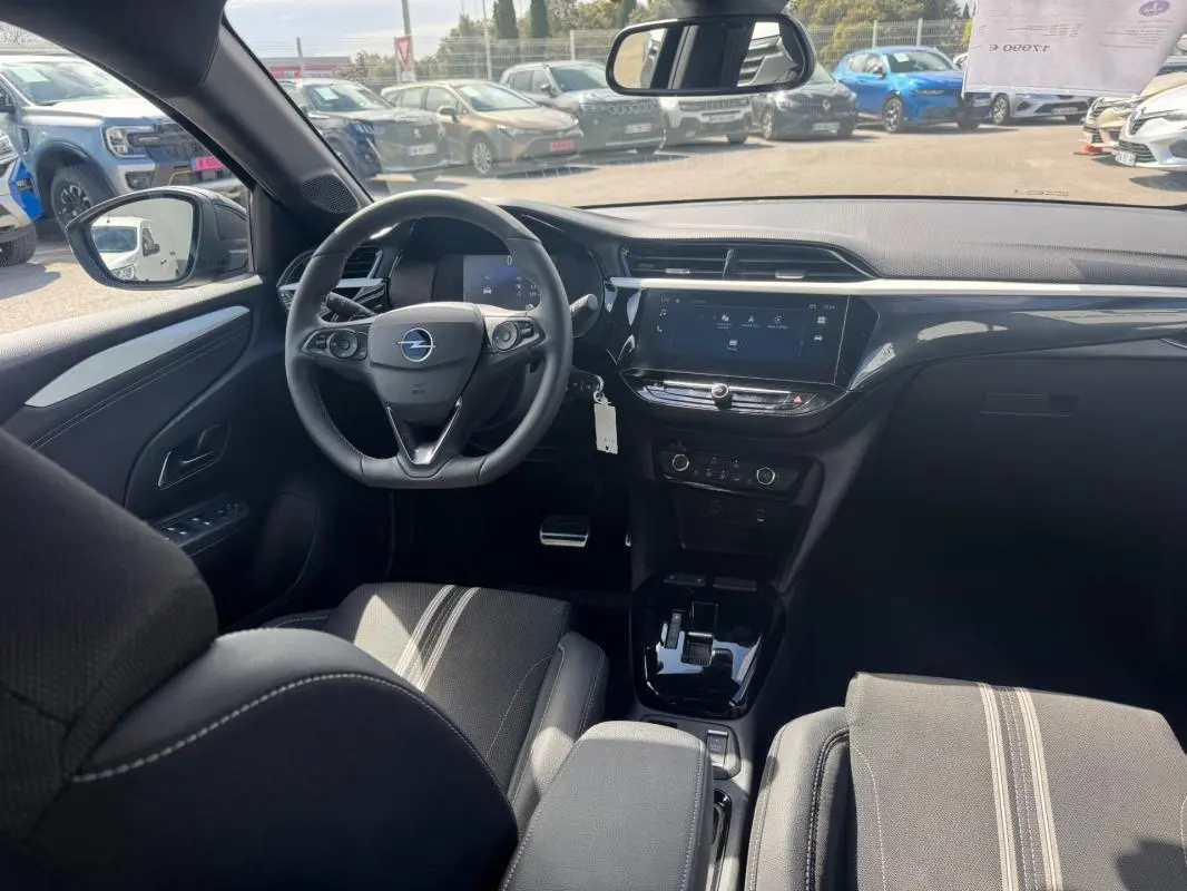Vue intérieure avant de l’Opel Corsa 2025 noire, montrant le volant, la console centrale avec écran tactile et les sièges tissu à bandes claires.