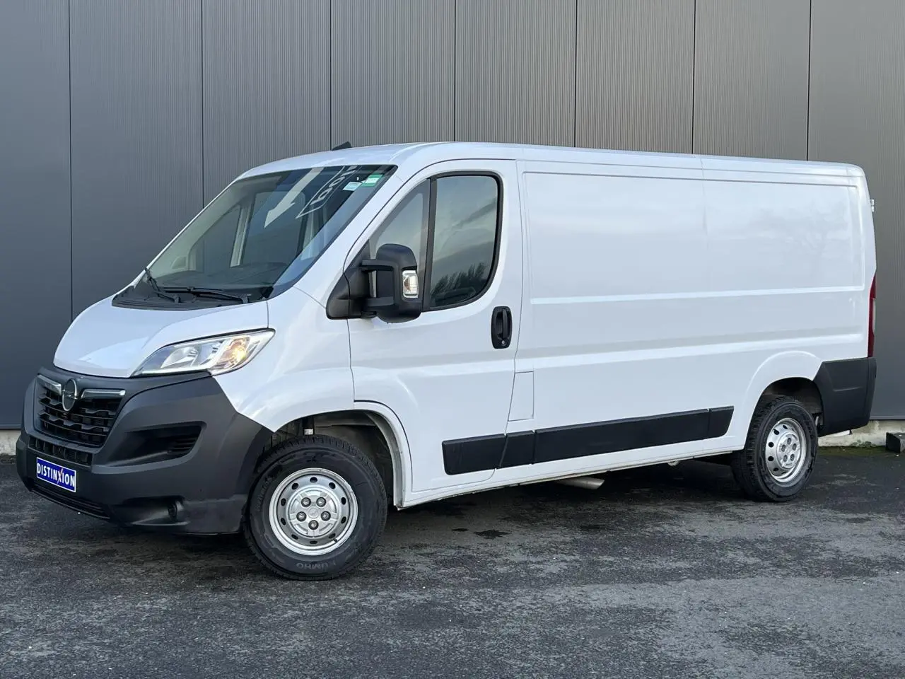 Vue 3/4 avant droit d’un Opel Movano Fourgon blanc avec pare-chocs noirs et porte latérale coulissante droite.