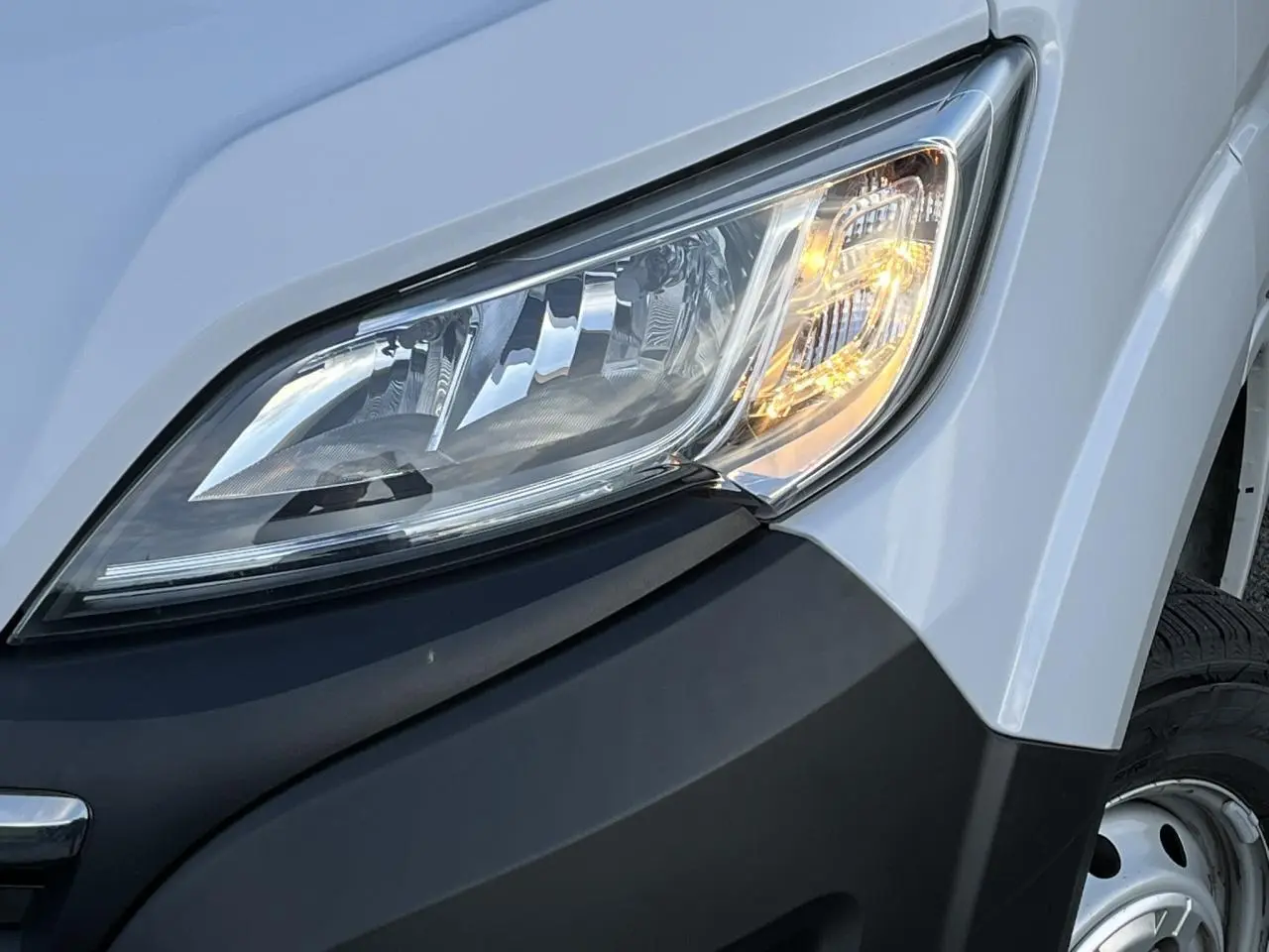Gros plan sur le phare avant droit d’un Opel Movano Fourgon blanc avec pare-chocs noir et roue acier visible.
