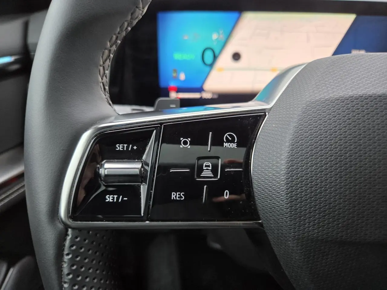 Gros plan sur les commandes gauche du volant noir du Renault Austral 2025 avec écran numérique flou en arrière-plan.