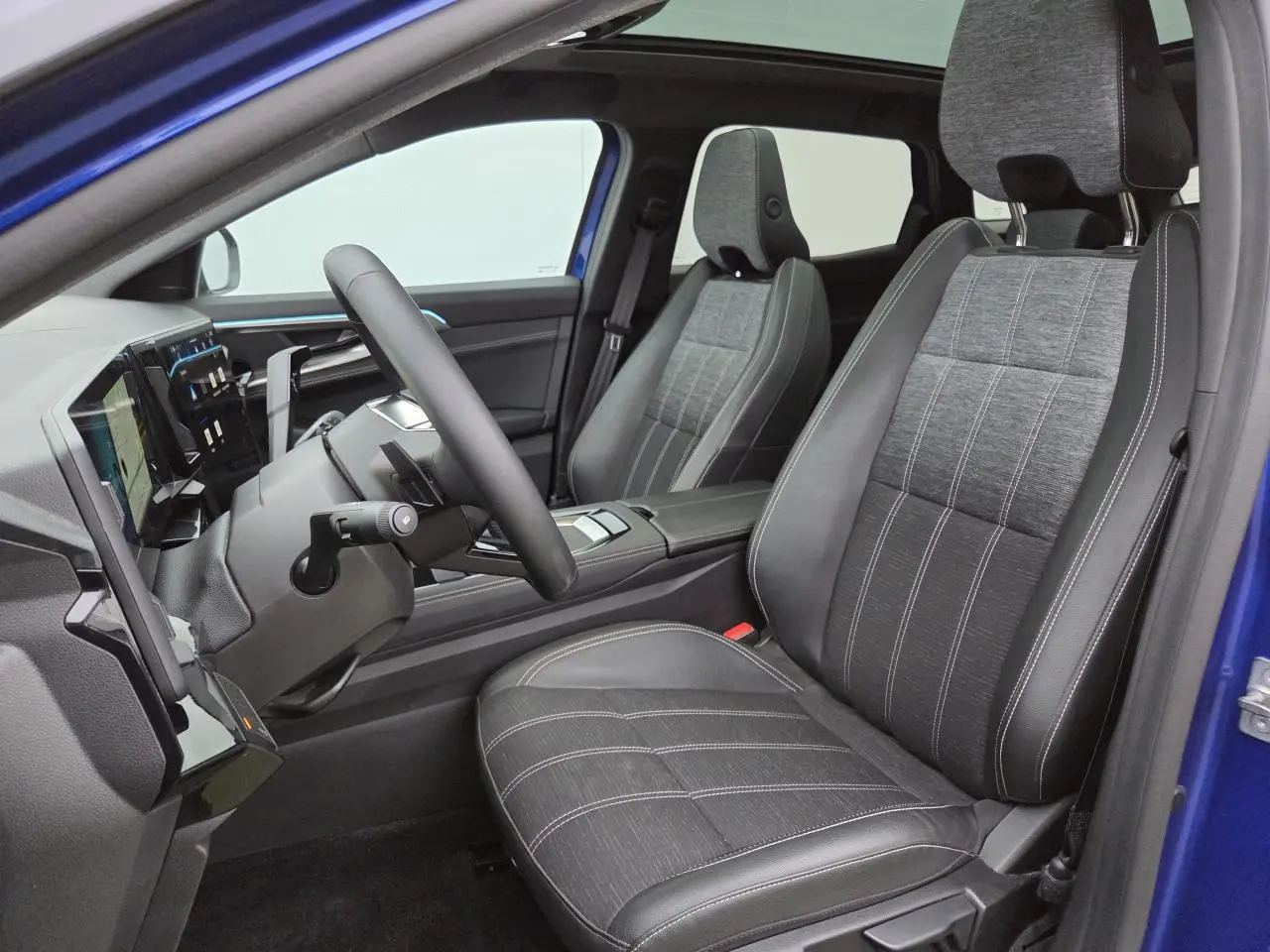 Vue intérieure côté conducteur du Renault Austral E-Tech bleu Iron, sièges tissu et cuir noirs avec surpiqûres blanches.