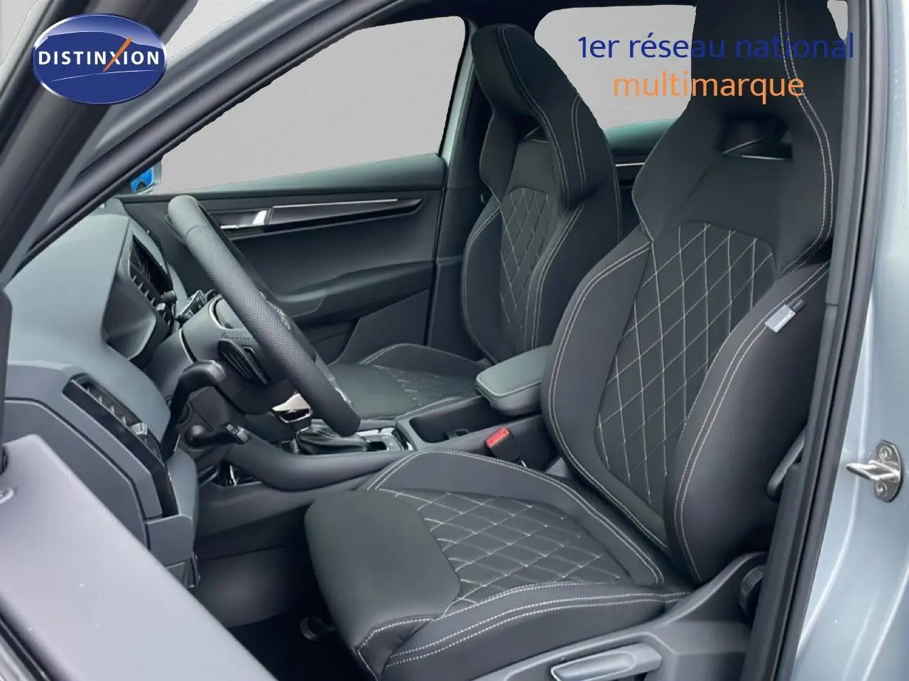 Vue intérieure côté conducteur du Skoda Karoq gris argent, sièges sport en tissu noir avec surpiqûres blanches.