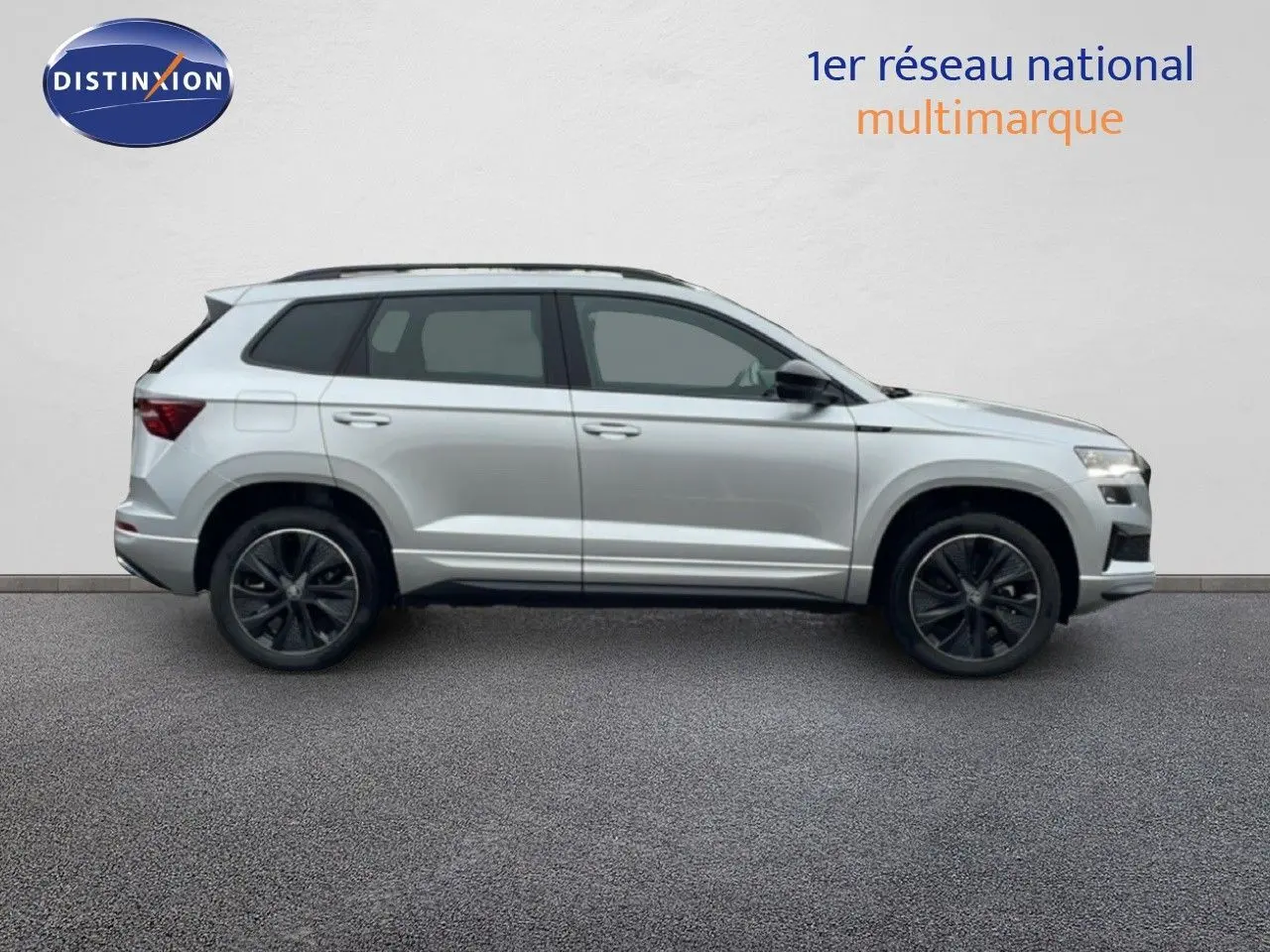 Vue de profil côté gauche d’un Skoda Karoq gris argent métallisé 2025 avec jantes noires bicolores et toit ouvrant.