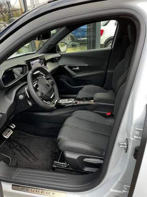 Vue intérieure côté conducteur du Peugeot 2008 blanc, mettant en valeur le tableau de bord numérique et les sièges en tissu noir.