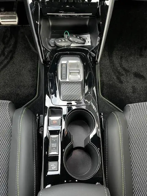 Vue plongeante sur la console centrale noire brillante du Peugeot 2008 GT 2024 avec commandes et porte-gobelets.