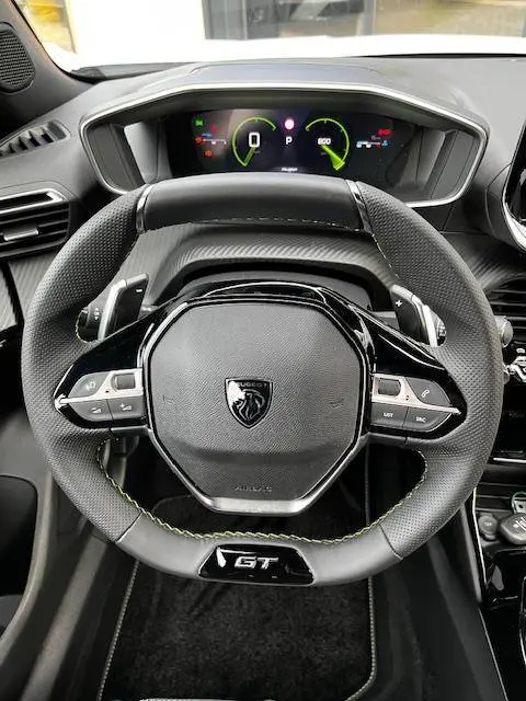 Vue rapprochée du volant GT noir avec surpiqûres vertes et tableau de bord numérique du Peugeot 2008 PureTech 130 2024.
