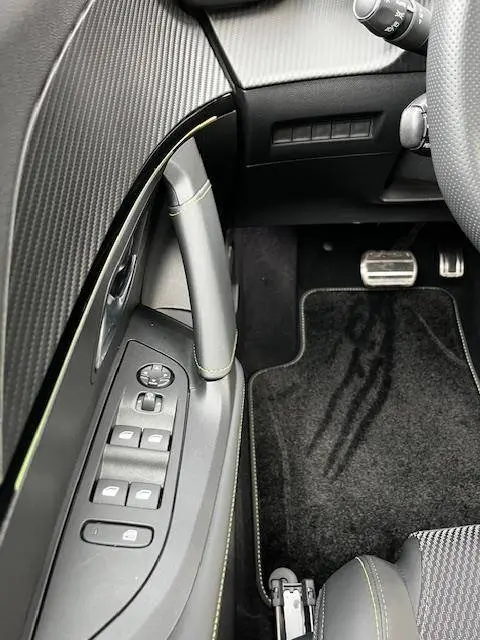 Vue intérieure côté gauche du Peugeot 2008 blanc 2024, mettant en valeur les commandes de vitres et le pédalier en aluminium.