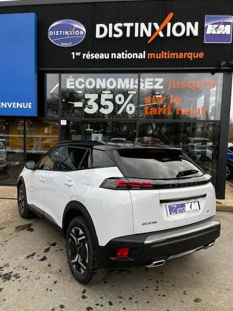 Vue 3/4 arrière droite d’un Peugeot 2008 blanc 2024 avec toit noir et feux arrière LED, devant une concession multimarque.