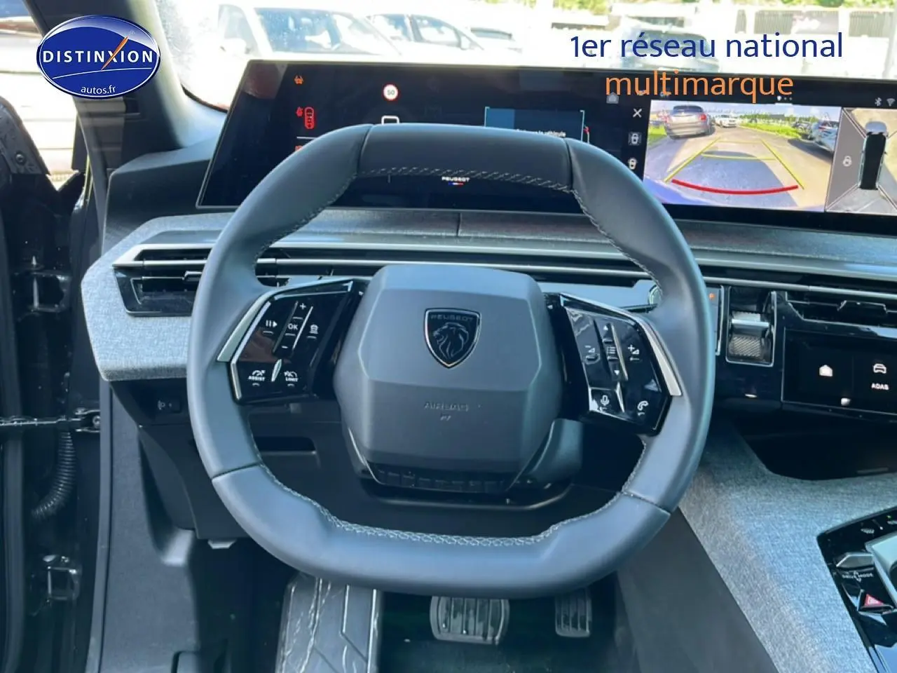 Vue intérieure centrée sur le volant cuir multifonction du Peugeot 5008 gris titane avec écran tactile et caméra de recul affichée.