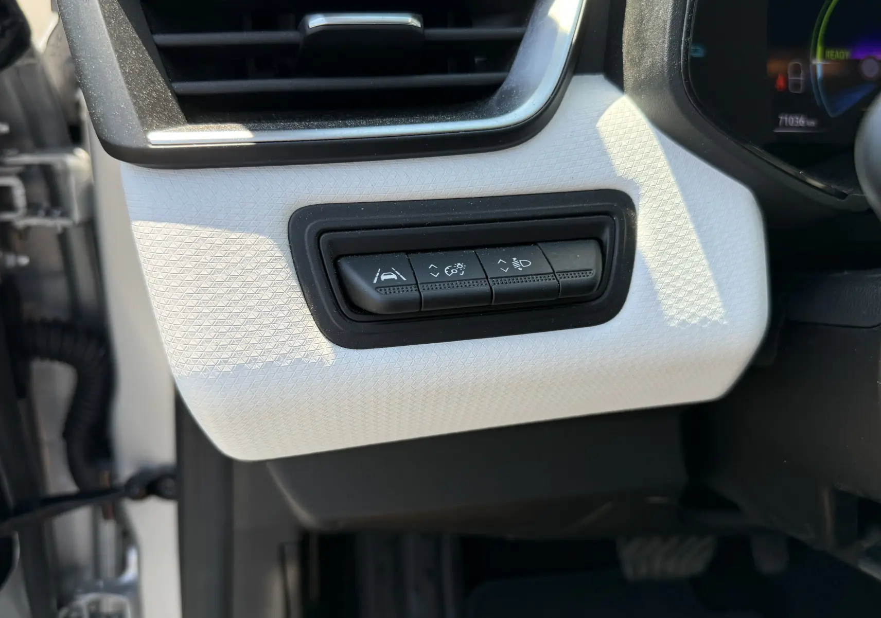 Gros plan sur les boutons de réglage d'assistance et d'éclairage à gauche du volant dans le tableau de bord gris clair d'une Renault Clio V hybride.