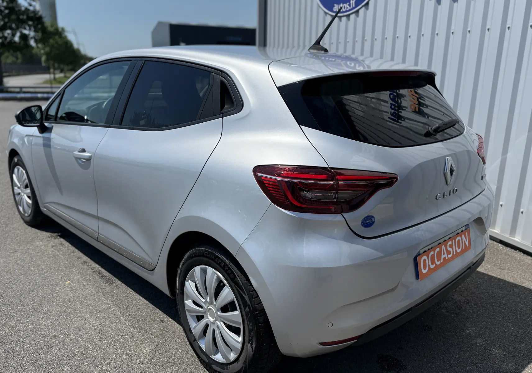 Vue 3/4 arrière droite d'une Renault Clio V grise, avec feux arrière LED et plaque "OCCASION" visible.