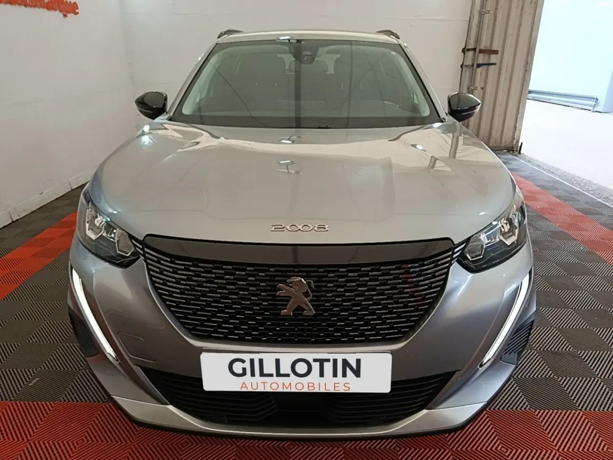 Vue avant d'un Peugeot 2008 gris clair avec calandre noire et feux LED en forme de griffes, dans un showroom.