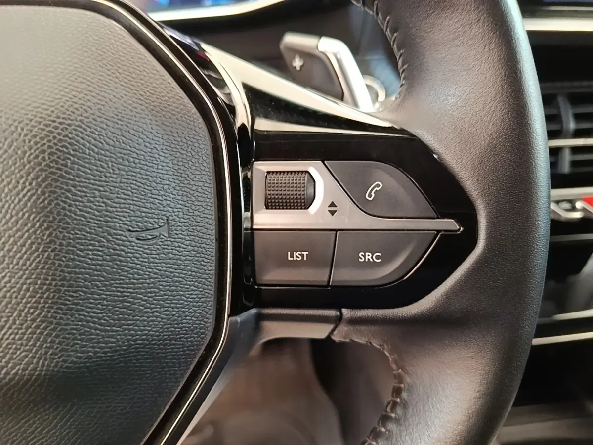 Gros plan sur les commandes gauche du volant cuir noir du Peugeot 2008, boutons de gestion audio et appel.