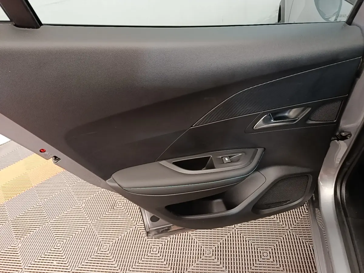 Porte intérieure côté gauche d’un Peugeot 2008 gris clair, avec garniture noire et surpiqûres bleues.