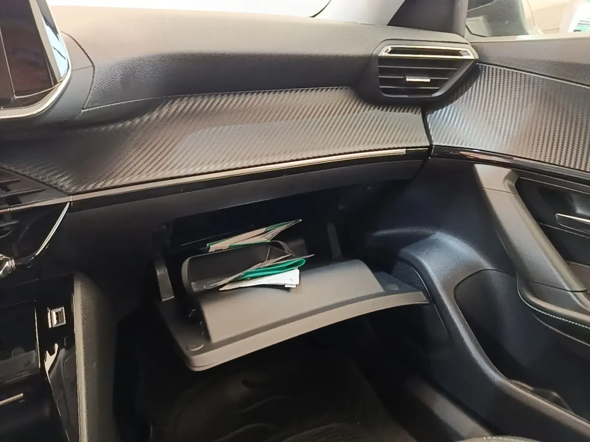 Vue intérieure côté passager du tableau de bord noir avec boîte à gants ouverte et finition effet carbone sur Peugeot 2008 gris clair.