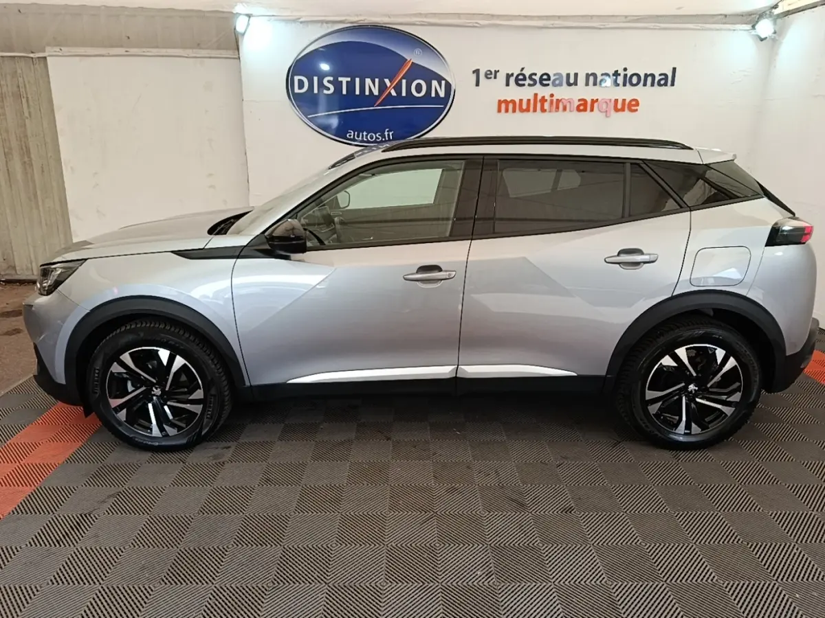 Vue latérale droite d’un Peugeot 2008 gris clair 2022 avec jantes noires et toit noir, en intérieur showroom.