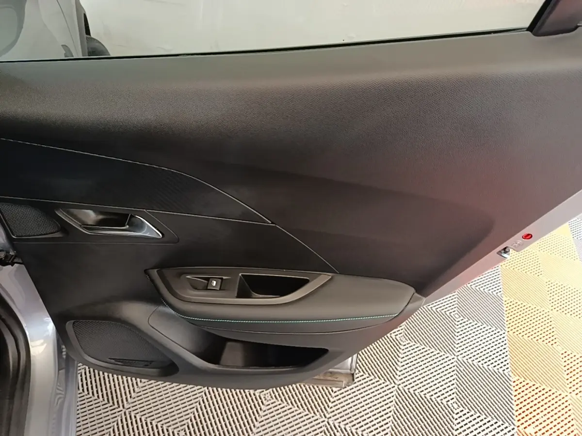 Vue intérieure du panneau de porte avant gauche gris clair du Peugeot 2008, avec commande de lève-vitre et poignée intégrée.