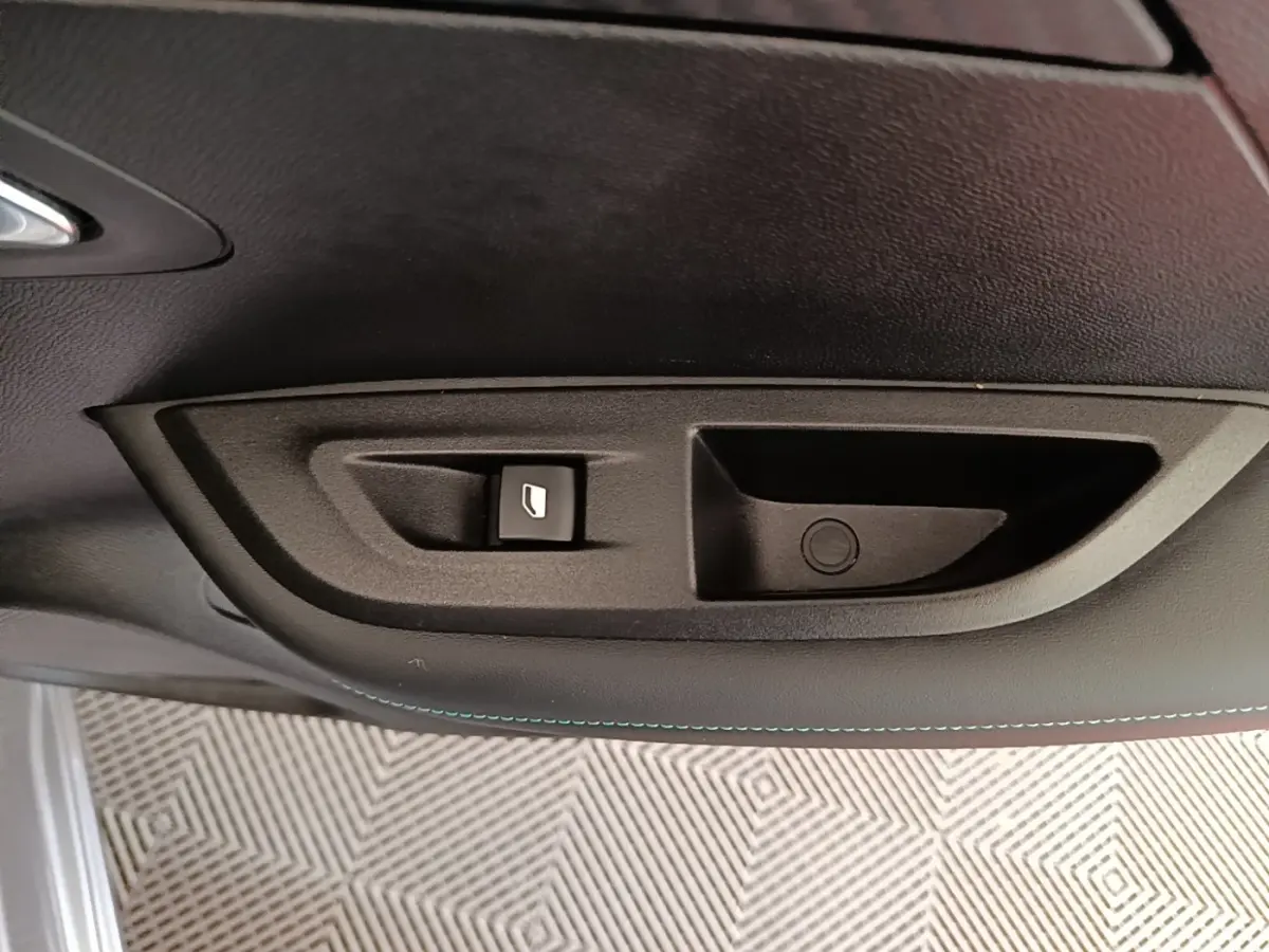 Détail de la commande de lève-vitre électrique sur la porte intérieure côté conducteur d’un Peugeot 2008 gris clair.