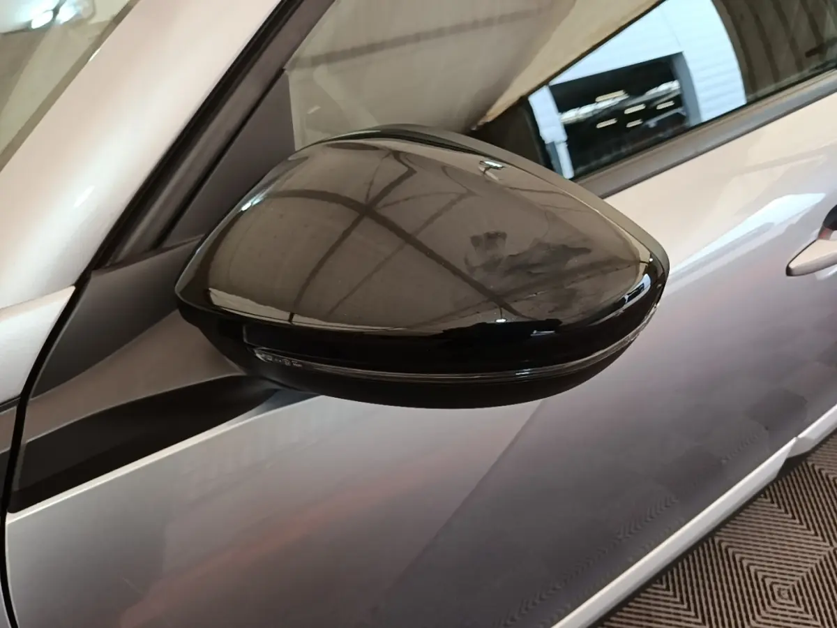 Gros plan sur le rétroviseur droit noir brillant du Peugeot 2008 gris clair, avec reflet de l'éclairage intérieur.