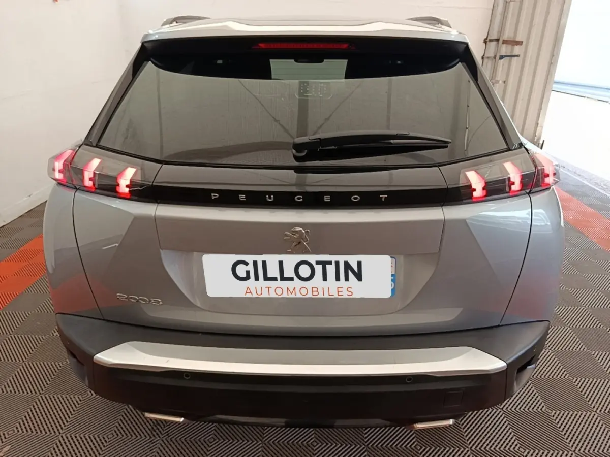 Vue arrière du Peugeot 2008 gris clair 2022 avec feux LED allumés et logo Peugeot visible sur le hayon.