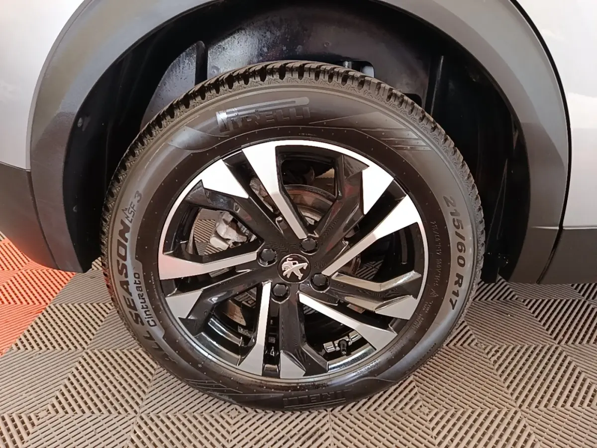 Gros plan sur la roue avant droite d’un Peugeot 2008 gris clair, jante alliage noir et argentée avec logo lion.