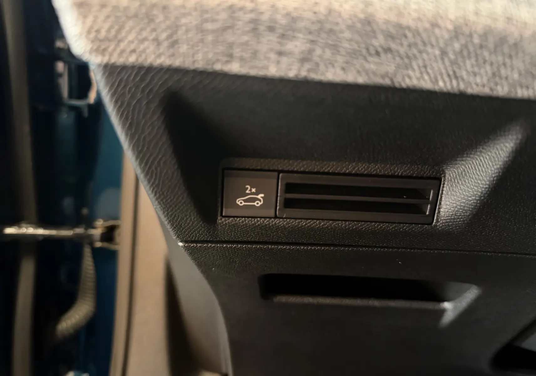 Détail intérieur montrant le bouton d'ouverture du hayon électrique sur la partie inférieure côté conducteur du Peugeot 3008 Bleu Obsession.