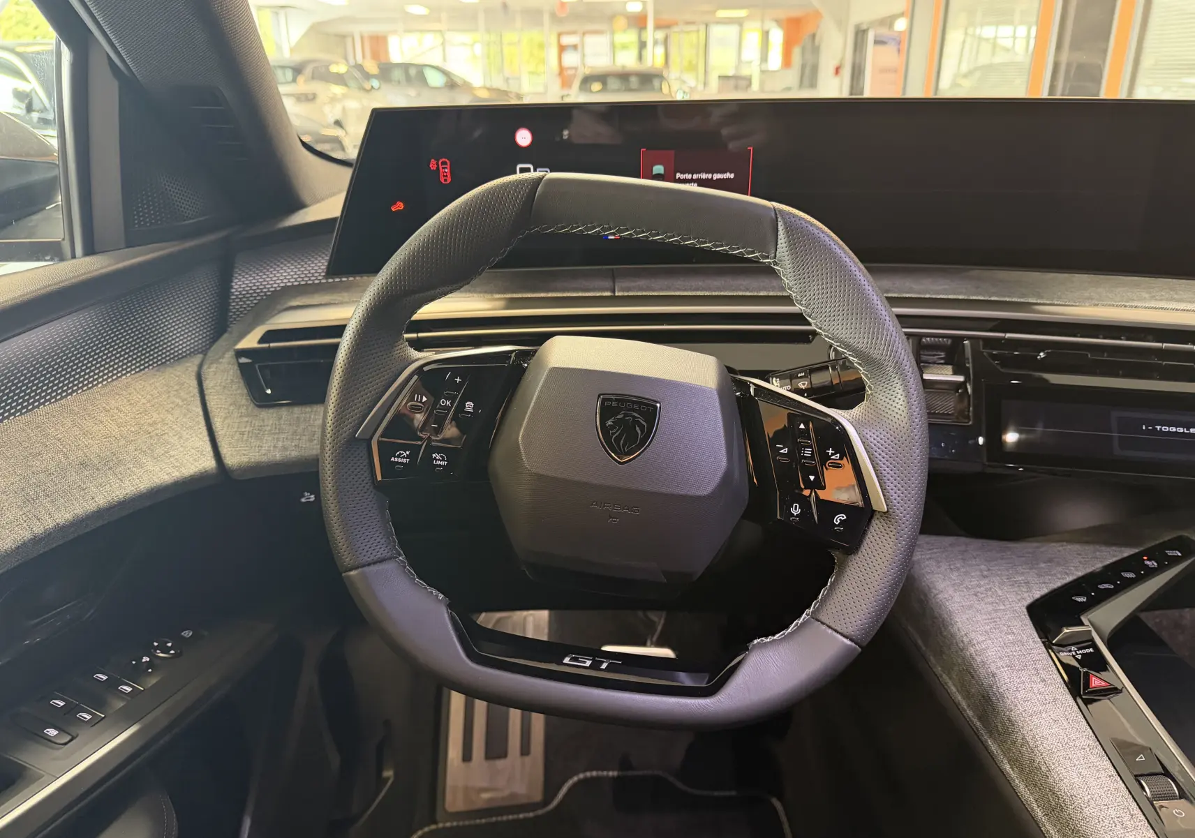 Vue intérieure centrée sur le volant GT du Peugeot 3008 Hybrid 145, avec tableau de bord numérique et habillage tissu gris.