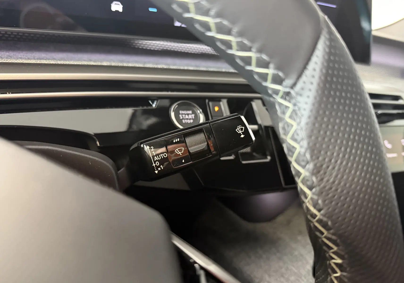 Gros plan sur la commande d’essuie-glace à gauche du volant perforé avec surpiqûres vert clair dans l’habitacle du Peugeot 3008 Hybrid 2025.