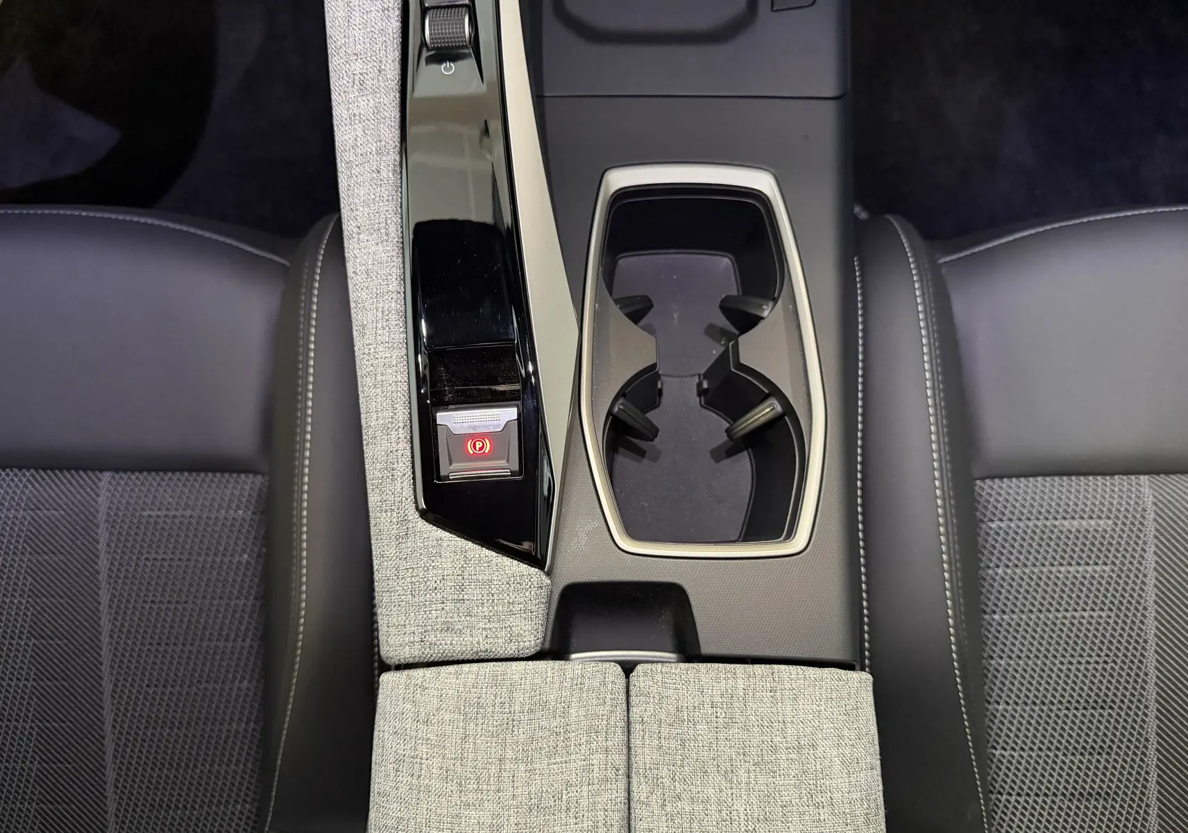 Vue plongeante sur la console centrale du Peugeot 3008 Hybrid 145 GT avec accoudoir tissu gris et porte-gobelets noirs.
