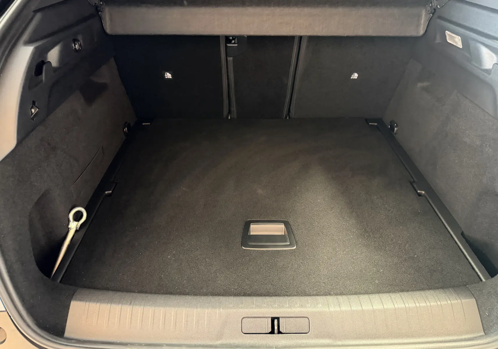 Coffre ouvert vu de l'arrière du Peugeot 3008 Hybrid 145 GT, espace de chargement propre et tapis noir.