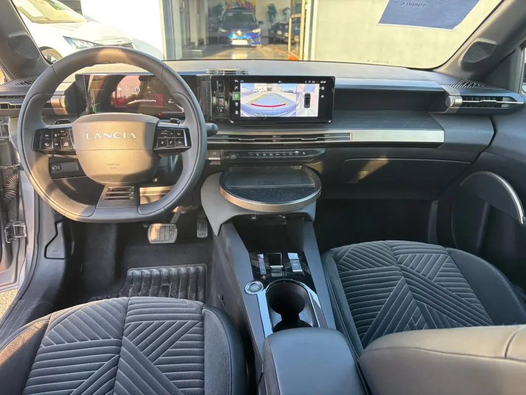 Vue intérieure avant de la Lancia Ypsilon 2025 gris, avec tableau de bord numérique et écran central affichant la caméra de recul.