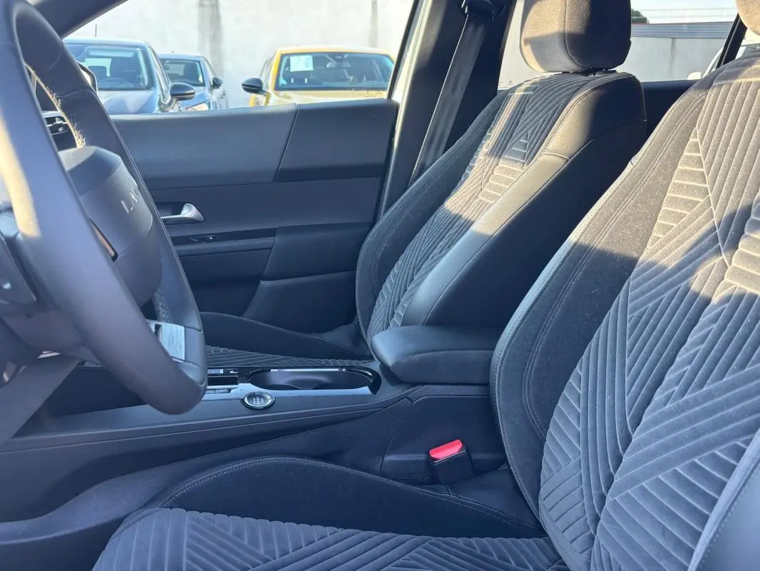 Vue intérieure côté conducteur de la Lancia Ypsilon 2025, montrant les sièges en tissu gris et le volant sport.