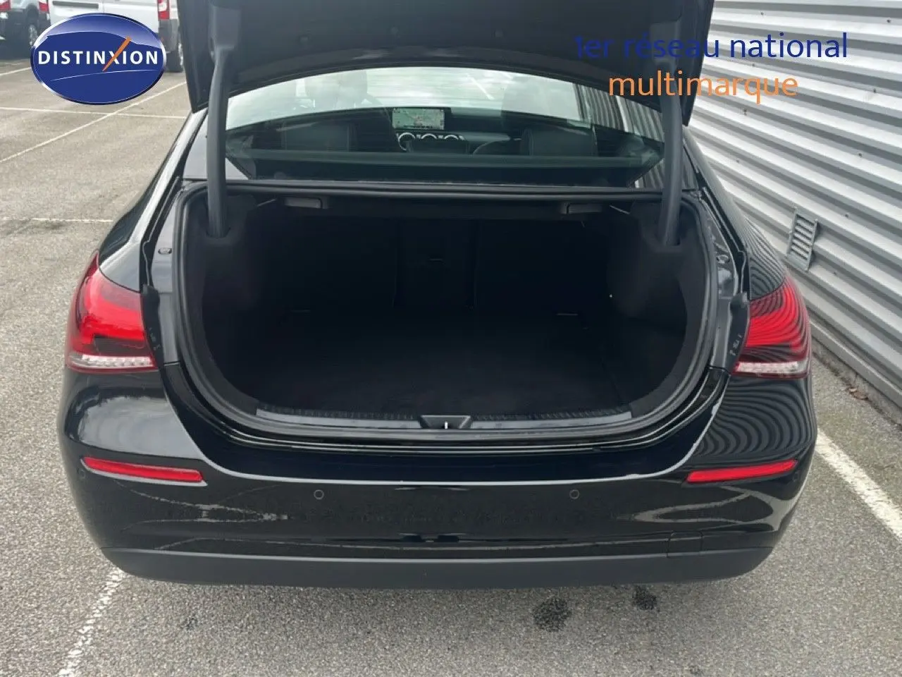 Vue arrière d'une Mercedes Classe A 180 Business Line noire Cosmos Metal avec coffre ouvert sur parking extérieur.