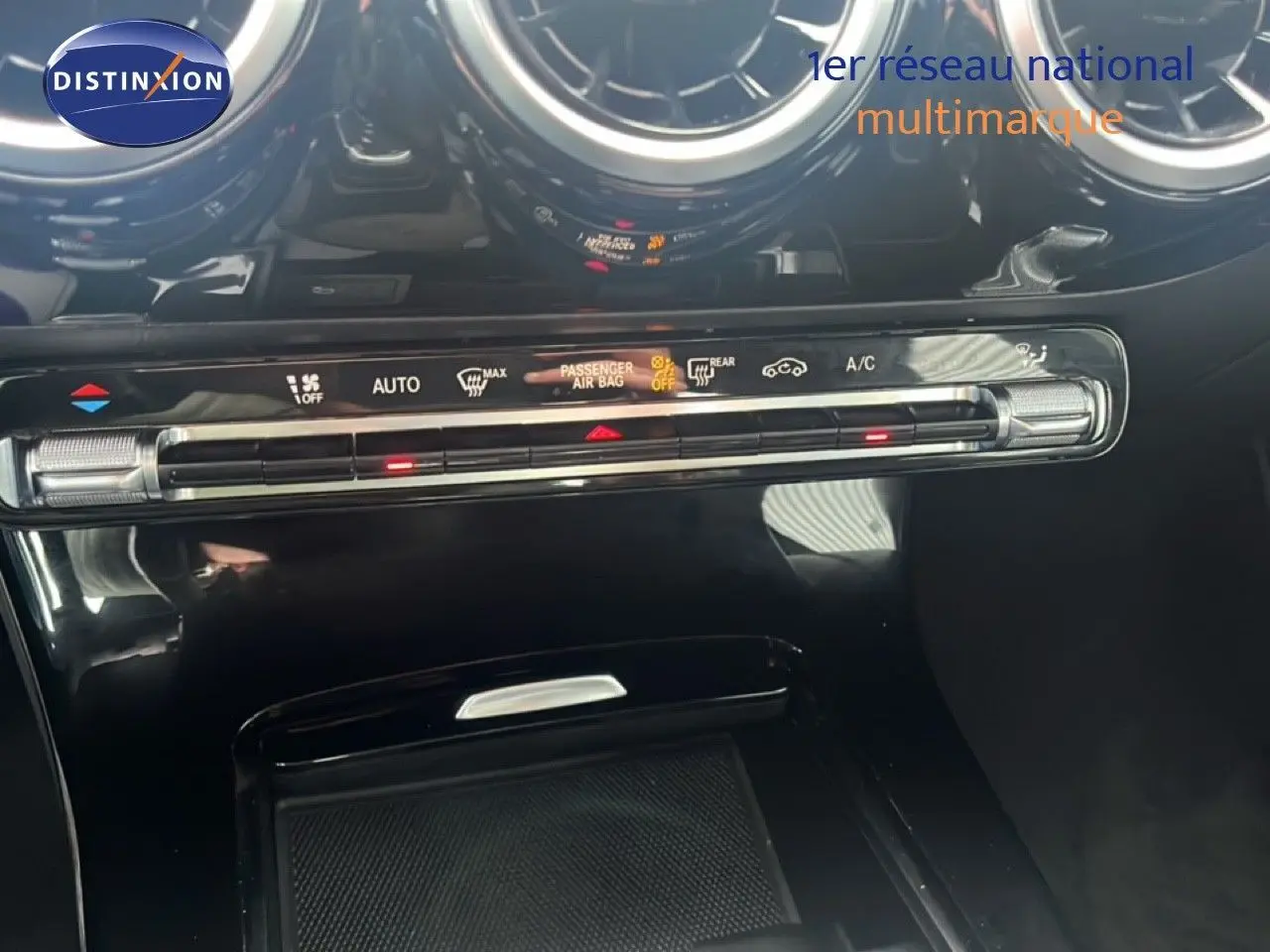 Gros plan sur la console centrale noire brillante de la Mercedes Classe A 180 Business Line avec commandes climatisation et aérateurs ronds.