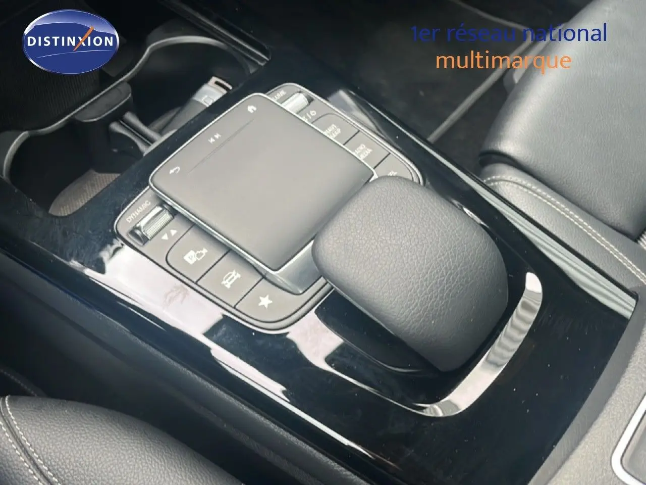 Gros plan sur la console centrale noire brillante de la Mercedes Classe A 180 Business Line avec pavé tactile et commandes intégrées.