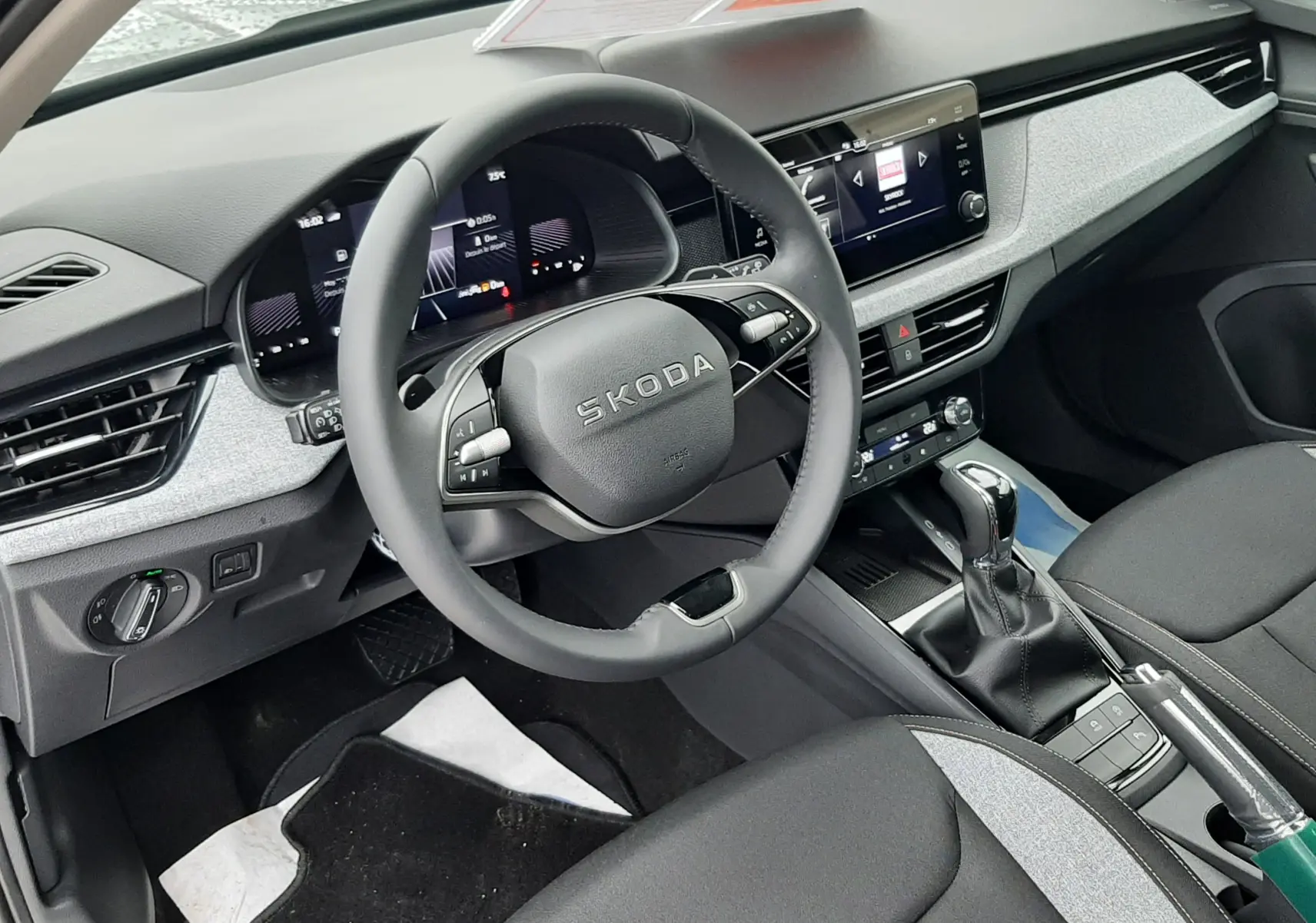 Intérieur du Skoda Kamiq 2025 vu côté conducteur, tableau de bord gris clair avec volant multifonction et sièges tissu noir et gris.