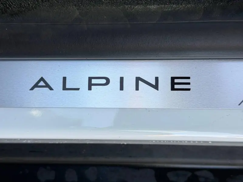 Gros plan sur la plaque de seuil de porte avec l'inscription Alpine sur un Renault Scénic blanc électrique 2025.