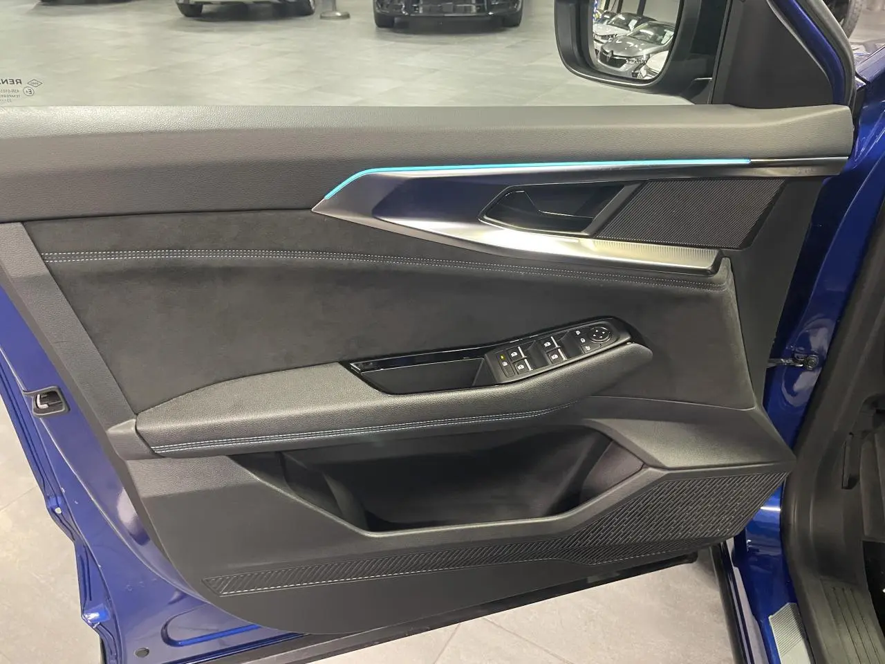 Vue côté gauche de la porte avant ouverte d’un Renault Austral 2024 bleu avec garniture Alcantara et commandes électriques.