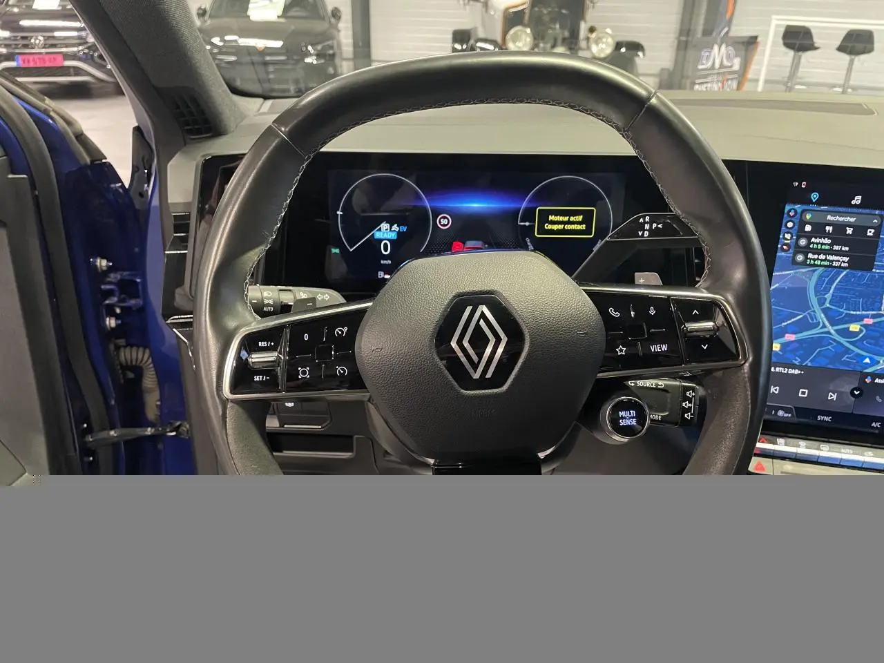 Vue intérieure centrée sur le volant noir avec logo Renault, tableau de bord numérique et écran tactile du Renault Austral Bleu Iron.